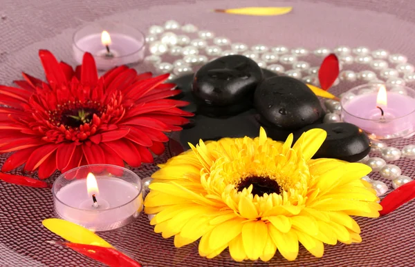 Pedras de spa com flores e velas em água na placa — Fotografia de Stock