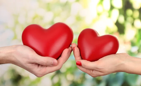 Corazones rojos en las manos de la mujer y del hombre, sobre fondo verde —  Fotos de Stock