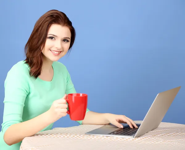 Mooie jonge vrouw die op laptop op blauwe achtergrond werkt — Stockfoto