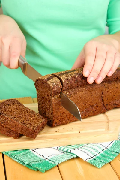 Woman slicing black bread on chopping board on wooden table close up — Stock Photo, Image