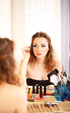 Genç ve güzel bir kadın aynanın yanında makyaj yapıyor.