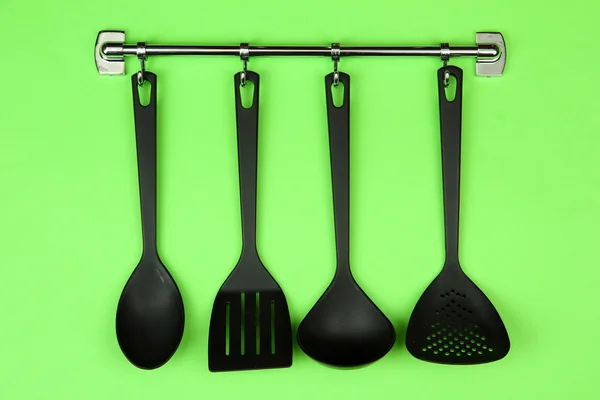 Sort køkkenredskaber på sølv kroge, på grøn baggrund - Stock-foto