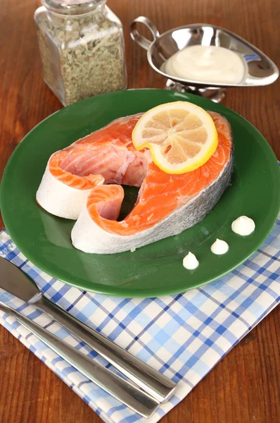 Stück roter Fisch auf Teller mit Gewürzen und Soße auf Holztisch in Großaufnahme — Stockfoto