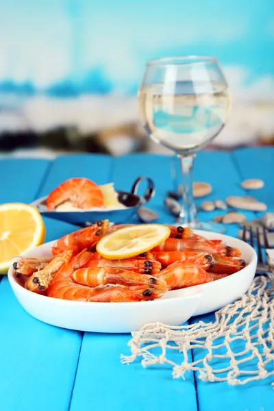Shrimps with lemon on plate on wooden table on blue natural background — Stock Photo, Image