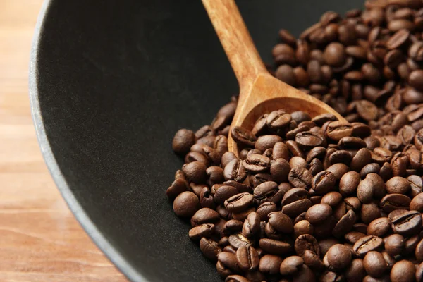 Black wok pan with coffee beans on wooden table, close up — Stock Photo, Image