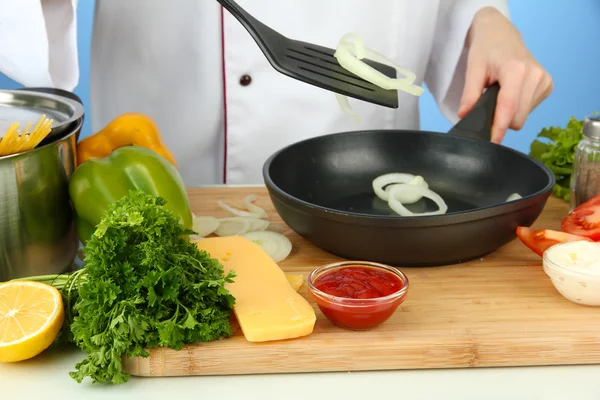 Hands prepare onion on pan, on blue background — Stock Photo, Image