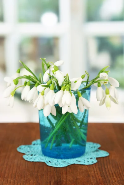 Kytice sněženka v skleněné vázy, na dřevěný stůl, světlé pozadí — Stock fotografie