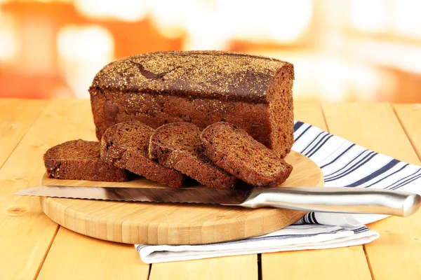 Sliced black bread and knife on chopping board on wooden table close up — Stock Photo, Image