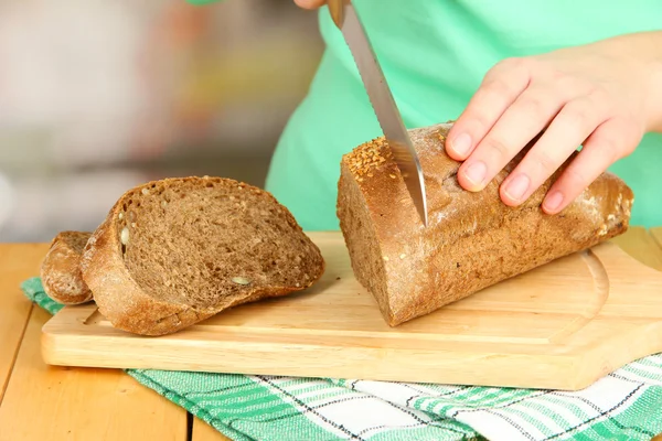 Woman slicing bread with sesame seeds on chopping board on wooden table close up — Stock Photo, Image