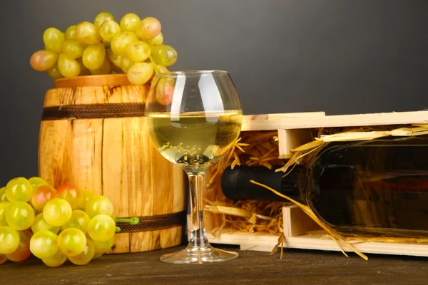 Dřevěné pouzdro s láhví vína, barel, skleničku a hroznů na dřevěný stůl na šedém pozadí — Stock fotografie