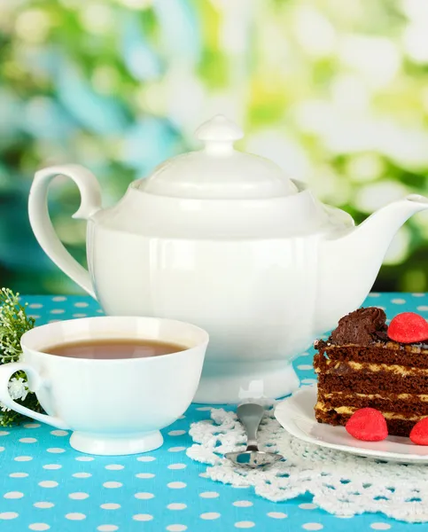 Tetera, taza de té y delicioso pastel sobre fondo natural —  Fotos de Stock