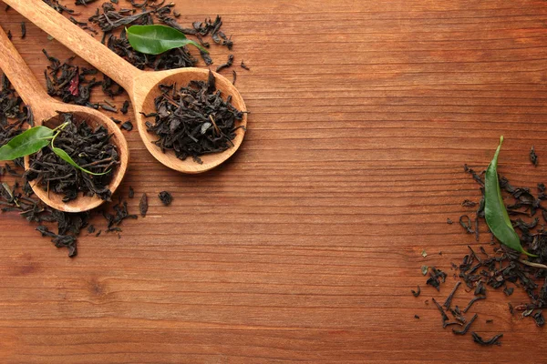 Té seco con hojas verdes en cucharas de madera, sobre fondo de madera — Foto de Stock