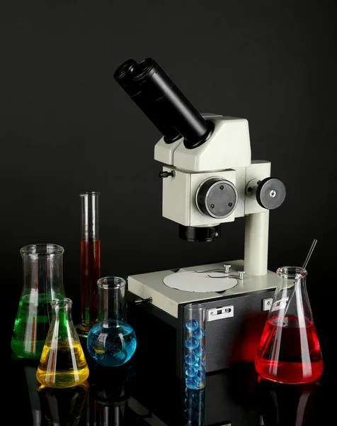 试管与多彩液体和显微镜上黑灰色的背景 — 图库照片
