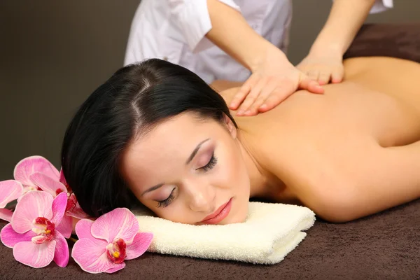 Hermosa joven en el salón de spa recibiendo masaje con piedras de spa, sobre fondo oscuro — Foto de Stock