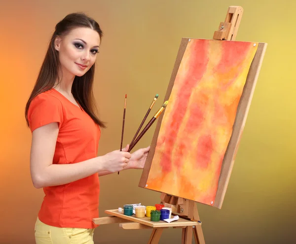 Beautiful young woman painter at work, on bright color background — Stock Photo, Image