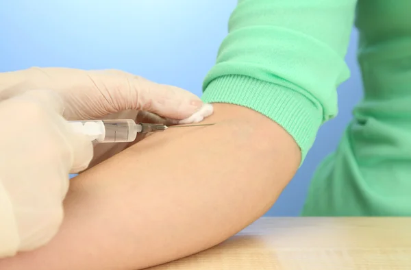Médico sosteniendo la jeringa con una vacuna en la mano del paciente, sobre fondo azul — Foto de Stock
