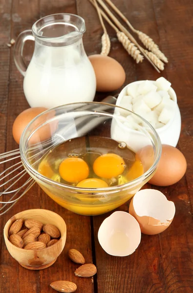 Uovo rotto in ciotola e vari ingredienti accanto a loro sul tavolo di legno primo piano — Foto Stock