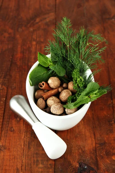 Herbs and spices in ceramic mortar, on wooden background — Stock Photo, Image