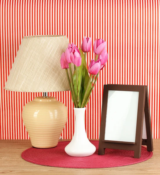 Marco de fotos marrón y lámpara sobre mesa de madera sobre fondo de pared rayado rojo — Foto de Stock