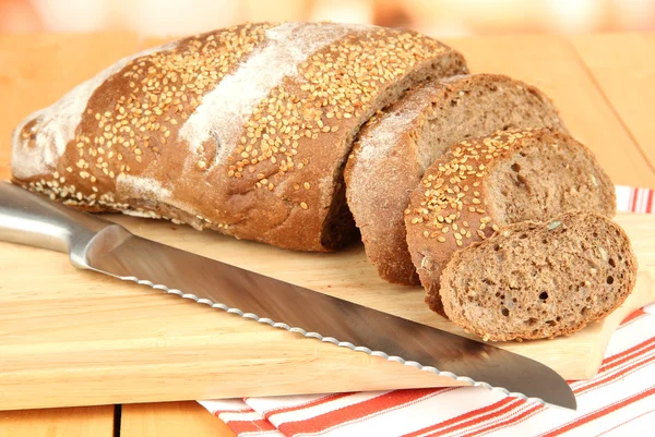 Pane affettato con semi di sesamo e coltello sul tagliere sul tavolo di legno da vicino — Foto Stock