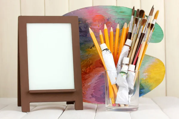 Photo frame as easel with artist's tools on wooden background — Stock Photo, Image