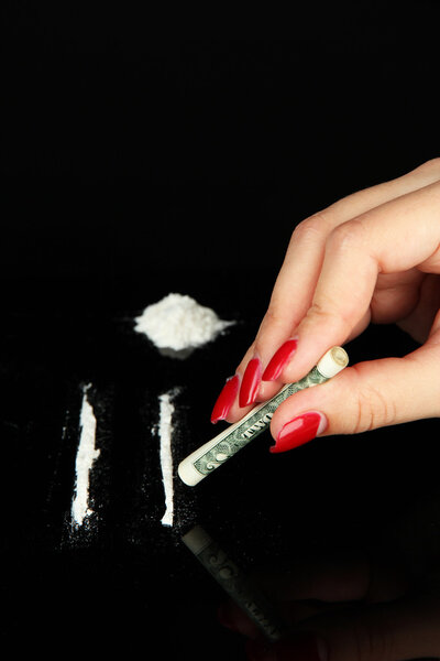 Cocaine drugs lines and female hand holding rolled dollar banknote, close up