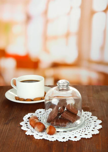 Pezzi di cioccolato sotto la copertura di vetro e bevanda calda su sfondo luminoso — Foto Stock
