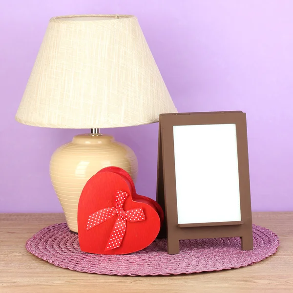 Brown photo frame and lamp on wooden table on lilac wall background — Stock Photo, Image