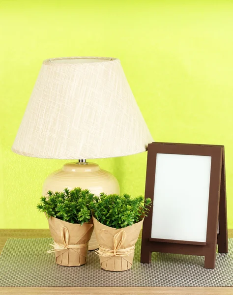 Marco de fotos marrón y lámpara sobre mesa de madera sobre fondo de pared verde — Foto de Stock