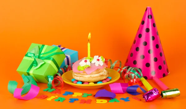 Bolo de aniversário colorido com vela e presentes no fundo laranja — Fotografia de Stock