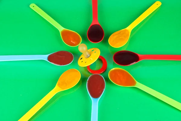 Puré de bebé en cucharas con pezón sobre fondo verde — Foto de Stock