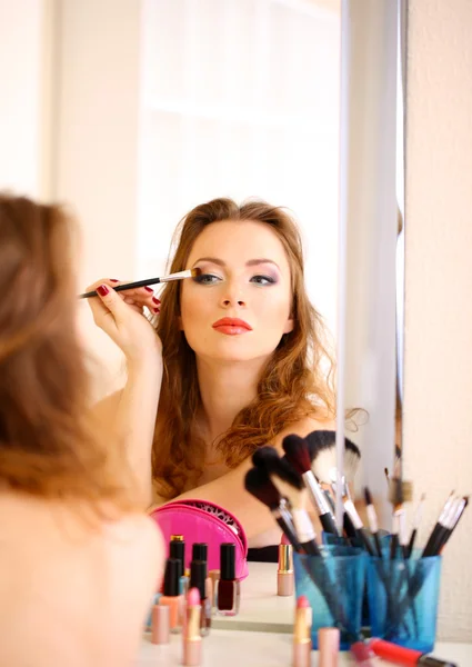 Joven hermosa mujer haciendo maquillaje cerca del espejo —  Fotos de Stock