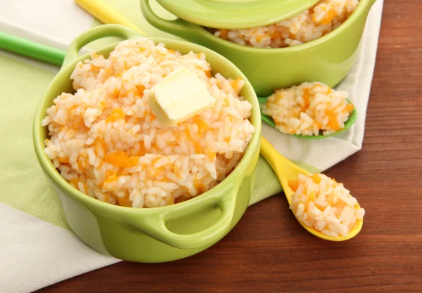 Taste rice porridge with pumpkin in saucepans on wooden background — Stock Photo, Image