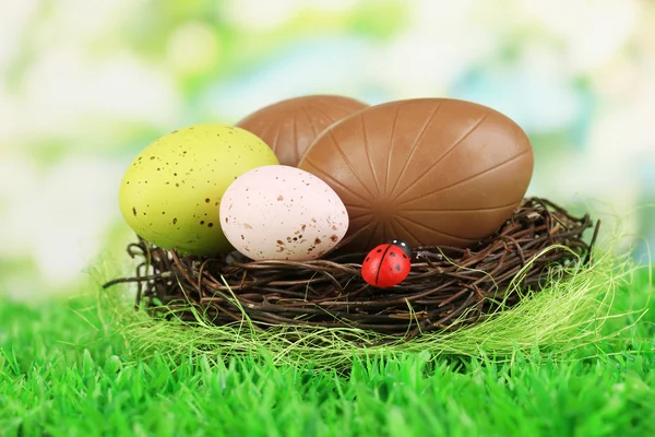 Composição de ovos de Páscoa e chocolate no ninho na grama no fundo natural — Fotografia de Stock
