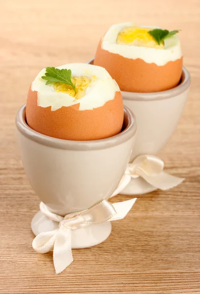 Boiled eggs in egg cups, on wooden table — Stock Photo, Image