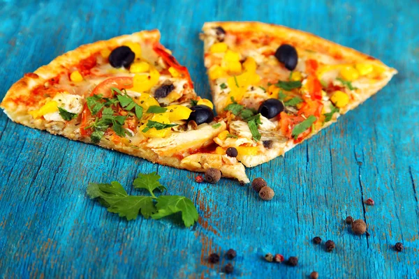 Segmenten van smakelijke pizza op blauwe houten tafel close-up — Stockfoto