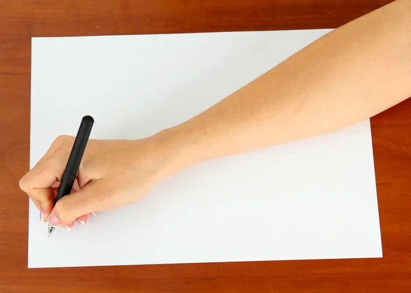 Hand with pen on white paper, on wooden background — Stock Photo, Image