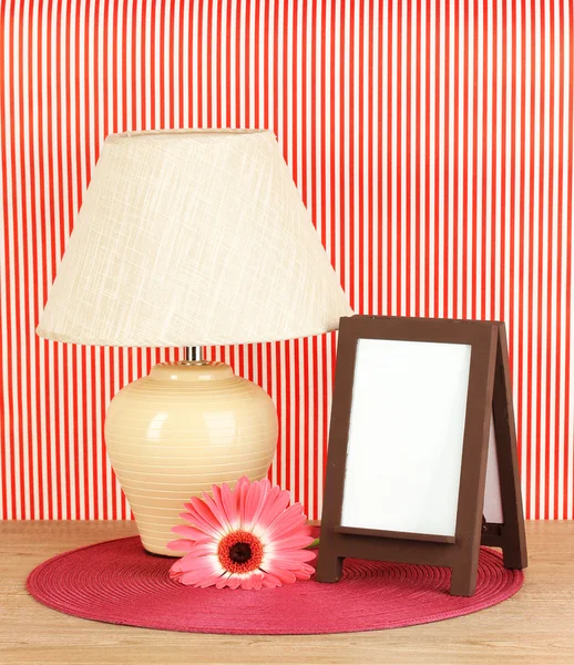 Marco de fotos marrón y lámpara sobre mesa de madera sobre fondo de pared rayado rojo —  Fotos de Stock