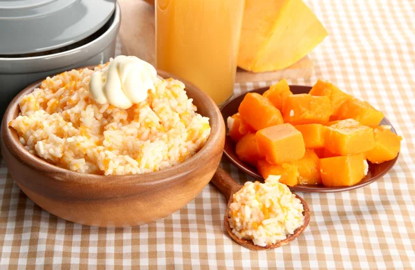 Taste rice porridge with pumpkin and glass of juice on tablecloth backgroun — Stock Photo, Image