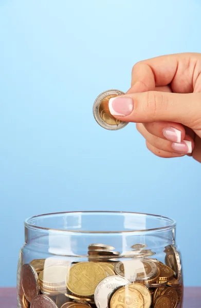 Ahorro, mano femenina poner una moneda en botella de vidrio, sobre fondo de color — Foto de Stock