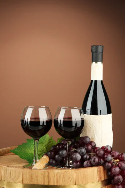 Σύνθεση των μπουκαλιών κρασιού, ποτήρια και σταφυλιών, σε ξύλινο βαρέλι, σε καφέ φόντο — Φωτογραφία Αρχείου
