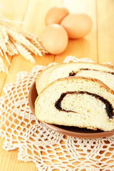 Loaf with poppy seeds on color plate, on wooden background — Stock Photo, Image