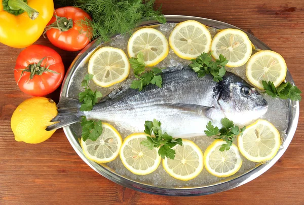 Pescado fresco de dorado en bandeja con limón y perejil sobre mesa de madera —  Fotos de Stock