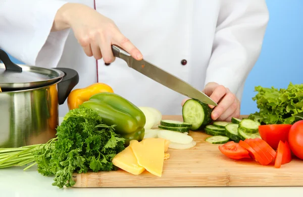 Mains féminines coupant des légumes, sur fond bleu — Photo