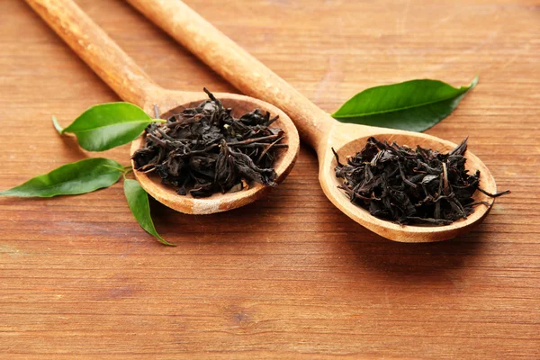 Tè secco con foglie verdi in cucchiai di legno, su sfondo di legno — Foto Stock