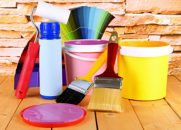 Paint pots, paintbrushes and coloured swatches on wooden table on stone wall background — Stock Photo, Image