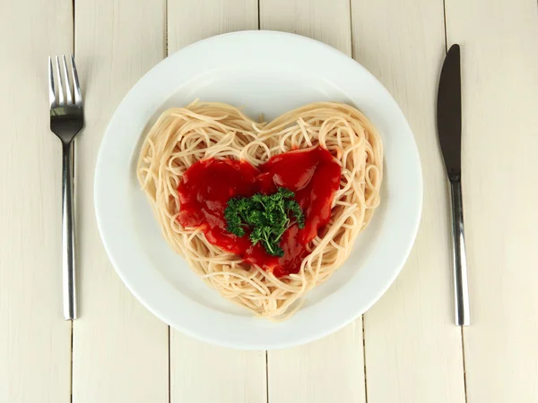 Spaghettis cuits soigneusement disposés en forme de coeur et garnis de sauce tomate, sur fond de bois — Photo