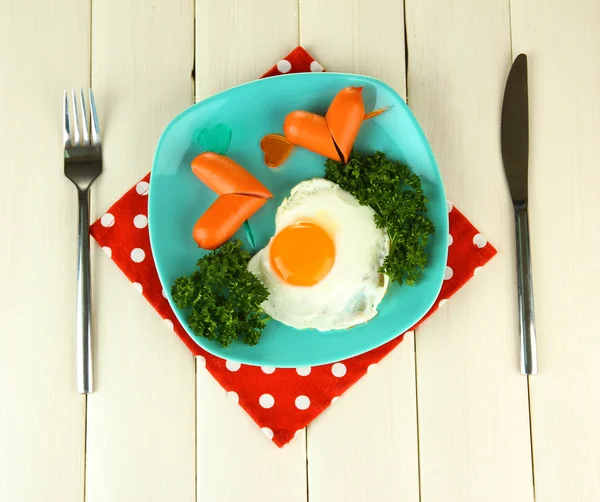 Sausages in form of hearts, scrambled eggs and parsley, on color plate, on wooden background — Stock Photo, Image