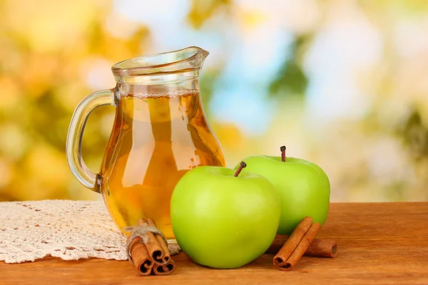 Plný džbán jablečné šťávy a apple na dřevěný stůl na světlé pozadí — Stock fotografie