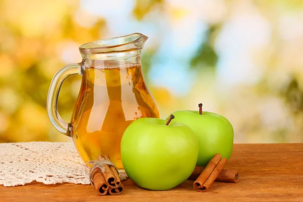 Jarra llena de zumo de manzana y manzana sobre mesa de madera sobre fondo brillante —  Fotos de Stock